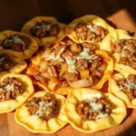 A close-up of a wooden table with a circular arrangement of stuffed pasta shells filled with a savory meat and vegetable mixture, topped with melted cheese.